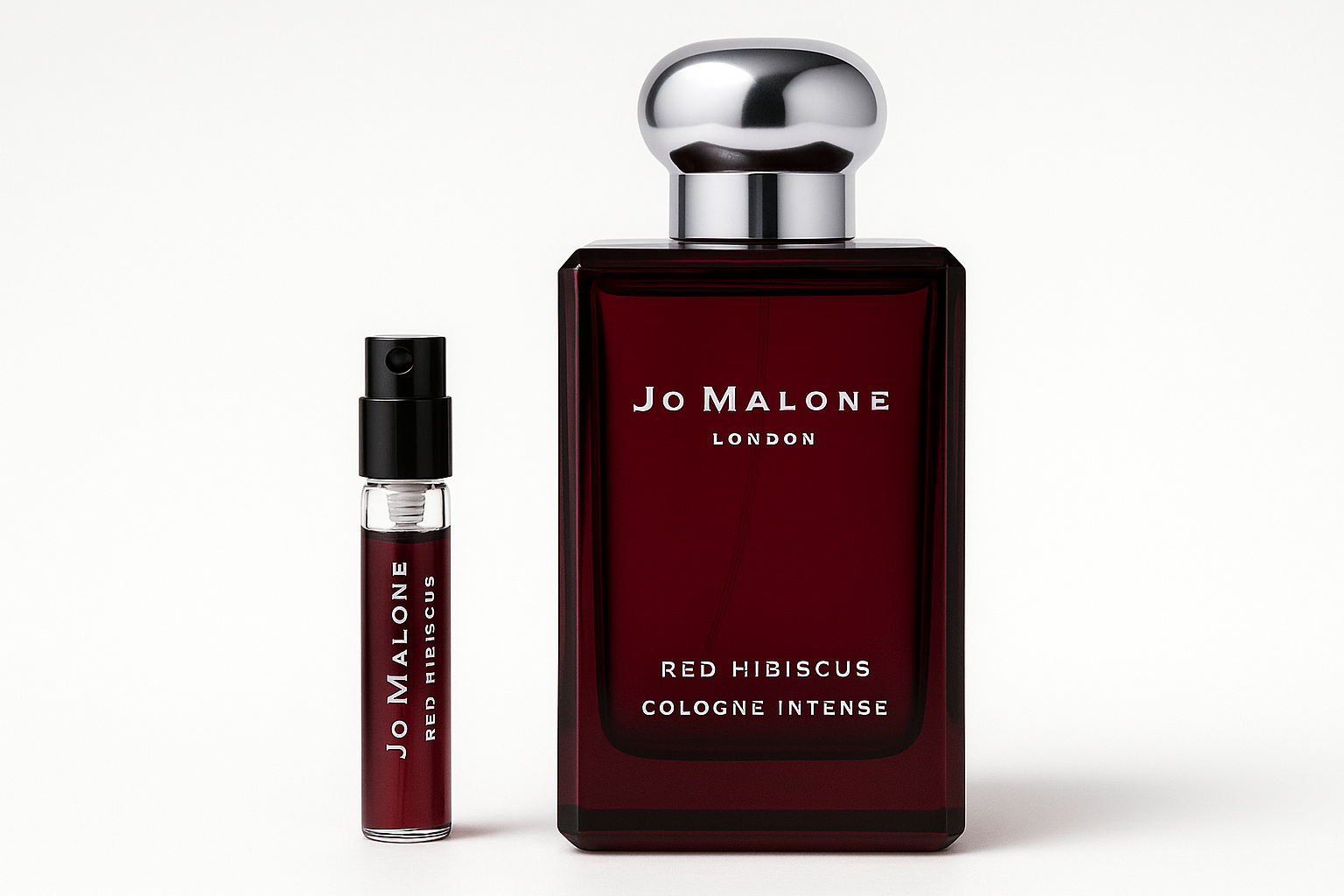 Jo Malone Red Hibiscus Cologne Intense דוגמית 2 מ"ל עומדת ליד בקבוק בושם 100 מ"ל של Jo Malone Red Hibiscus Cologne Intense עם כתובה לבנה על בקבוק אדום כהה
